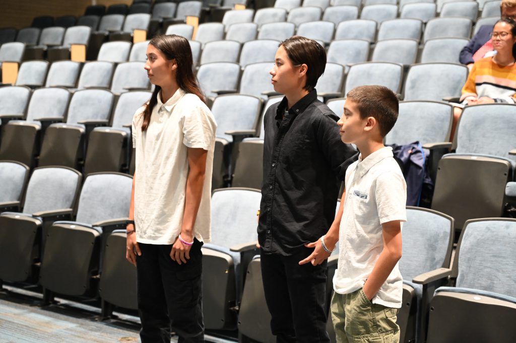 An image of the Miracle siblings standing at the front of the auditorium during a Board of Education meeting.