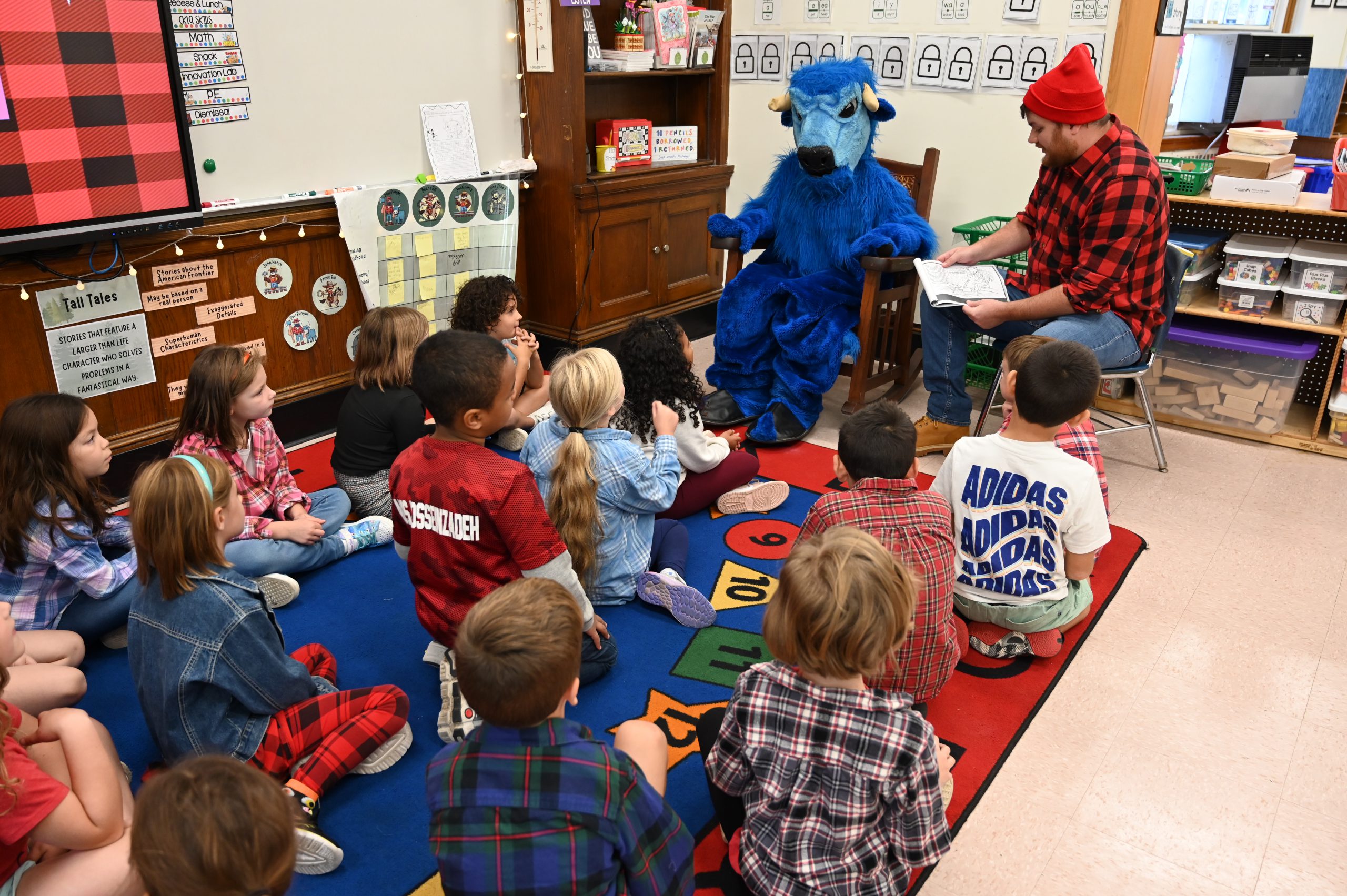 An image of Paul Bunyan and Babe the Ox sitting in front of a class of students, reading a book.