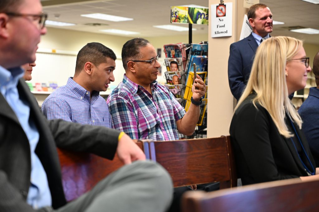 An image of a father and son looking on and recording on a phone.