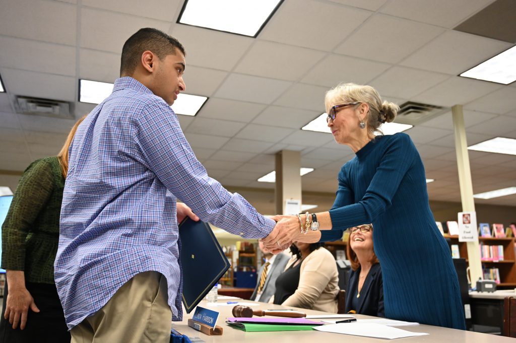 An image of a student shaking the hand of the North Colonie Board of Education President as he receives an award.