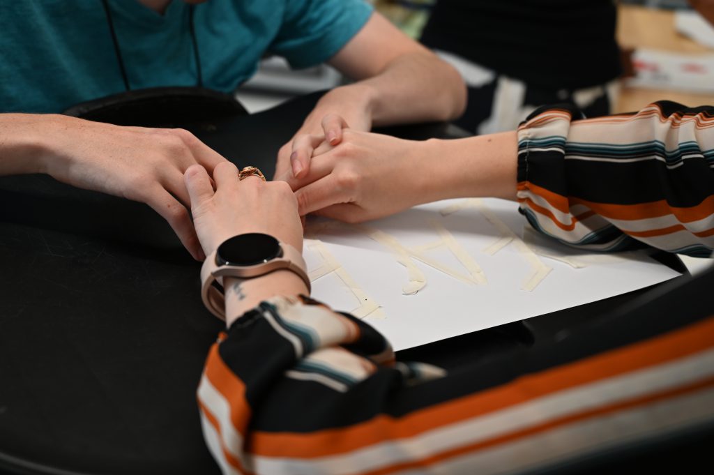 An image of two sets of hands working together on a project.