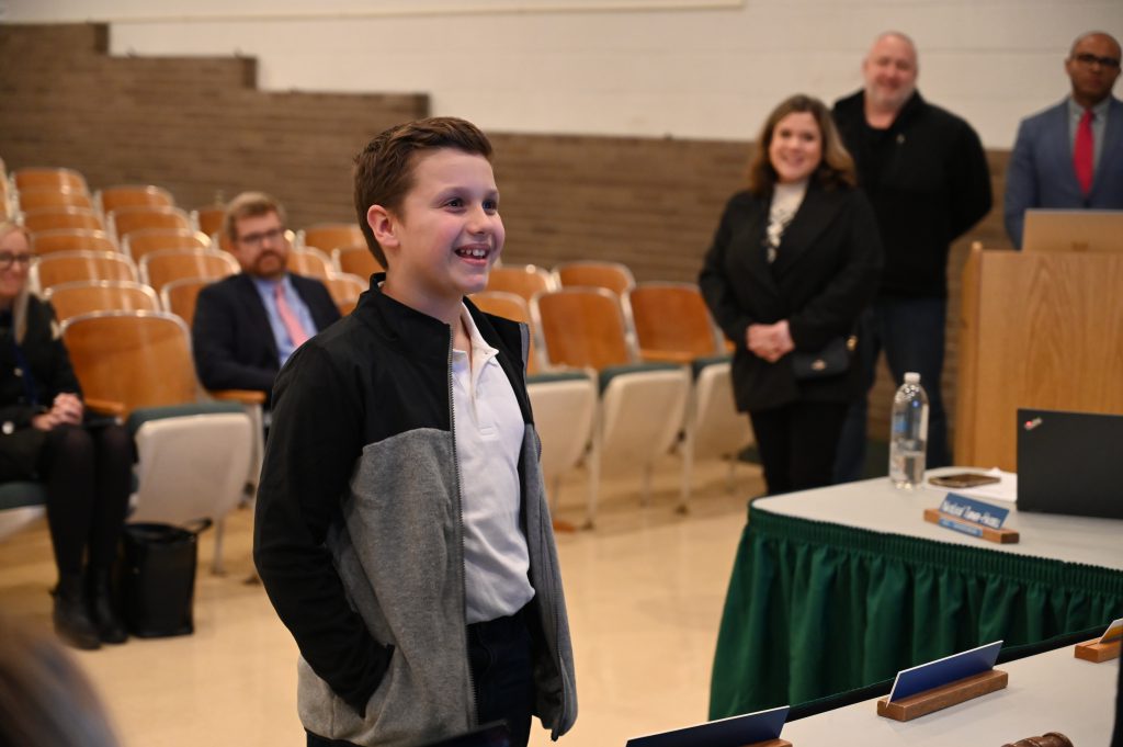 An image of a student smiling as he receives an award from Board of Education.