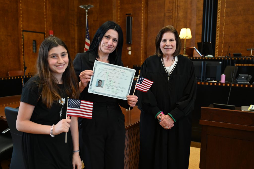 An image of a woman and her daughter posing with the judge as she received her certificate for citizenship.