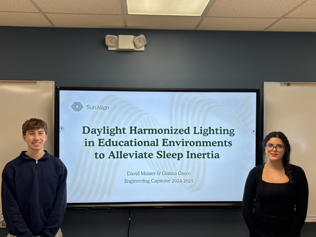 An image of two students standing in front of a title screen on their project.