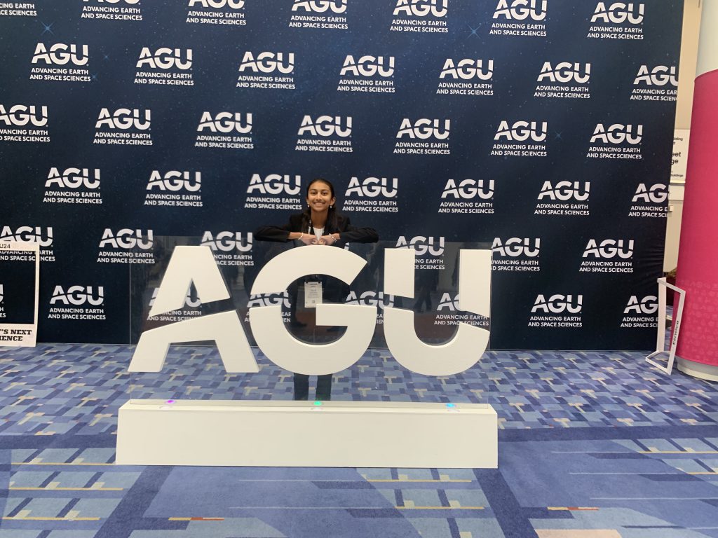 An image of a student standing behind an "AGU" sign or structure.