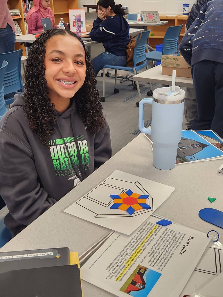 An image of a student smiling while showing off her barn quilt creation.