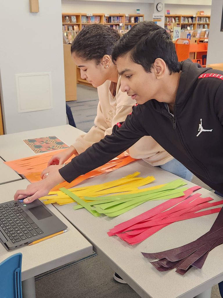 An image of students using a laptop to help them learn how to make kente cloths.