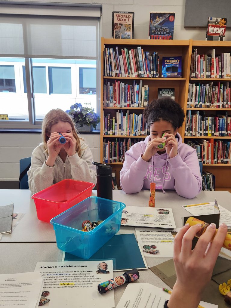 An image of two students looking through handmade kaleidoscopes.