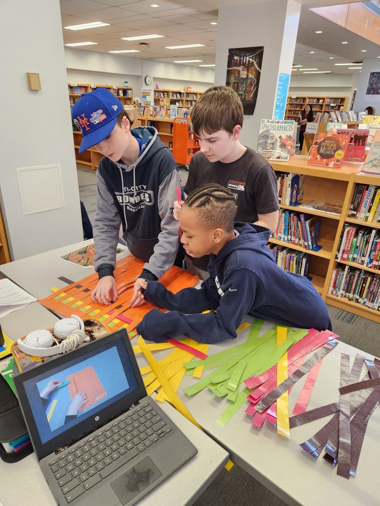 An image of three students weaving fabric to create kente cloths.