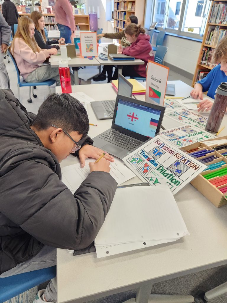 An image of a student writing with a pencil in front of a laptop.