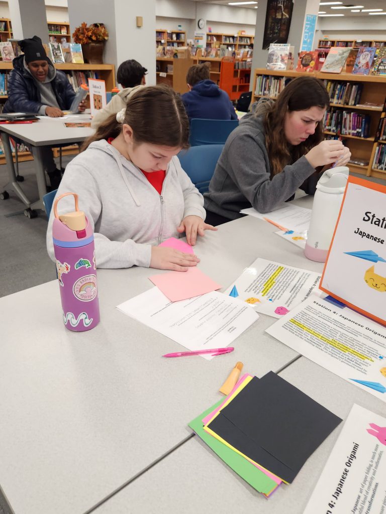 An image of two students folding paper to create origami.