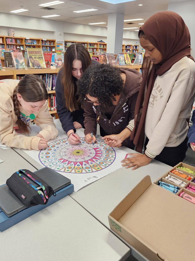 An image of four students standing around a table coloring a mandala.