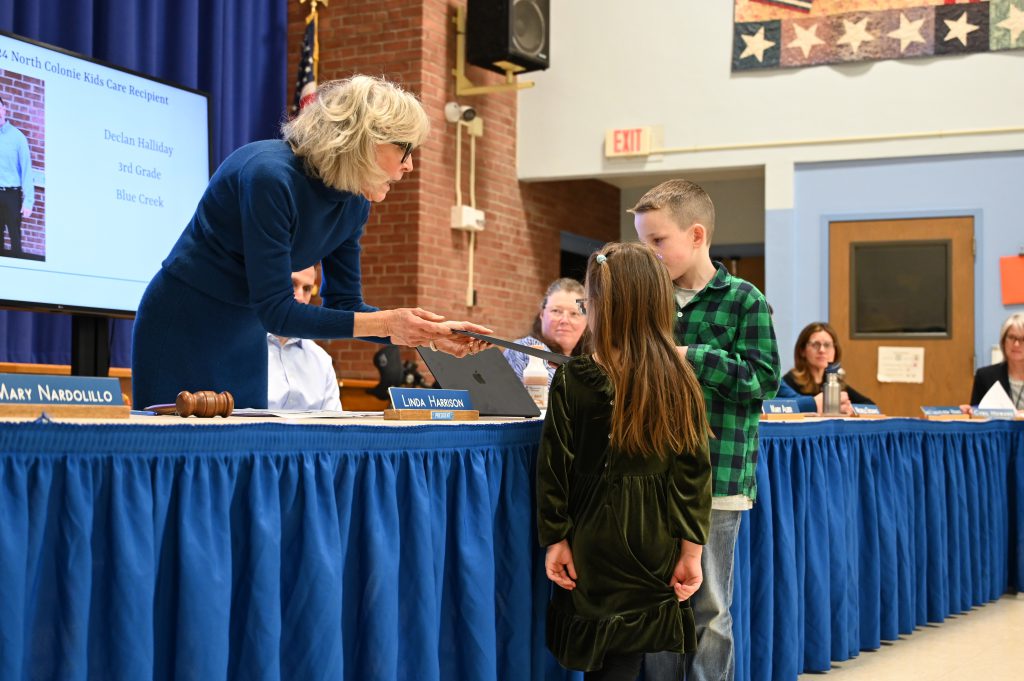 An image of a two students standing at a table as one receives a certificate.