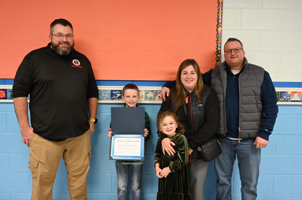 An image of a student holding a certificate surrounded by his family.