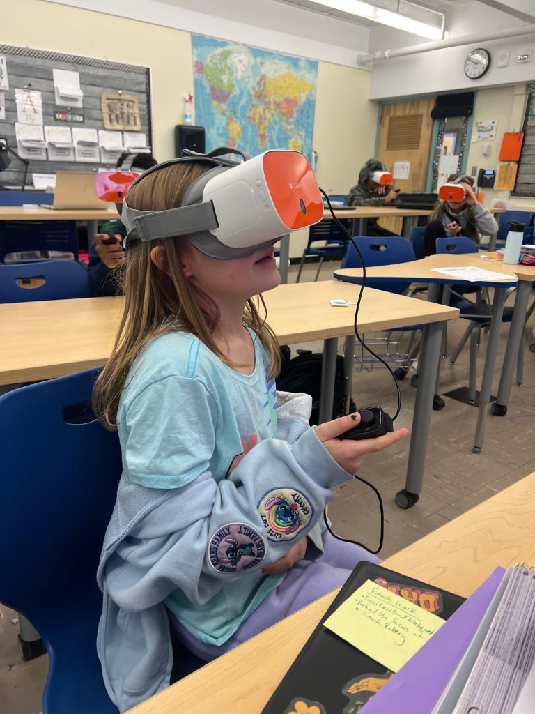 An image of a student with a virtual reality headset on and a remote control in her hand.