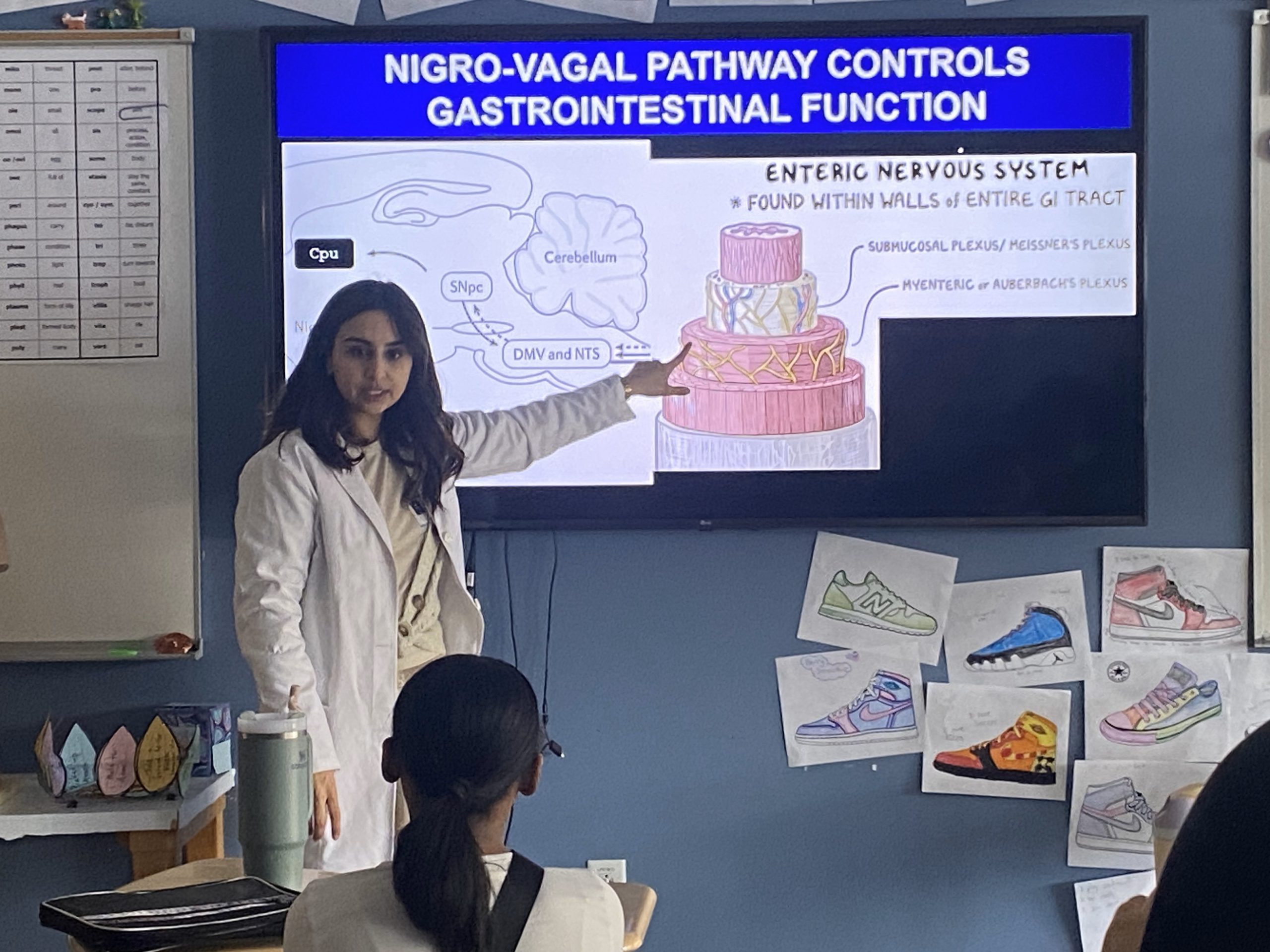 An image of Dr. Kainat Akhtar standing at the front of a classroom sharing her research on Parkinson's.