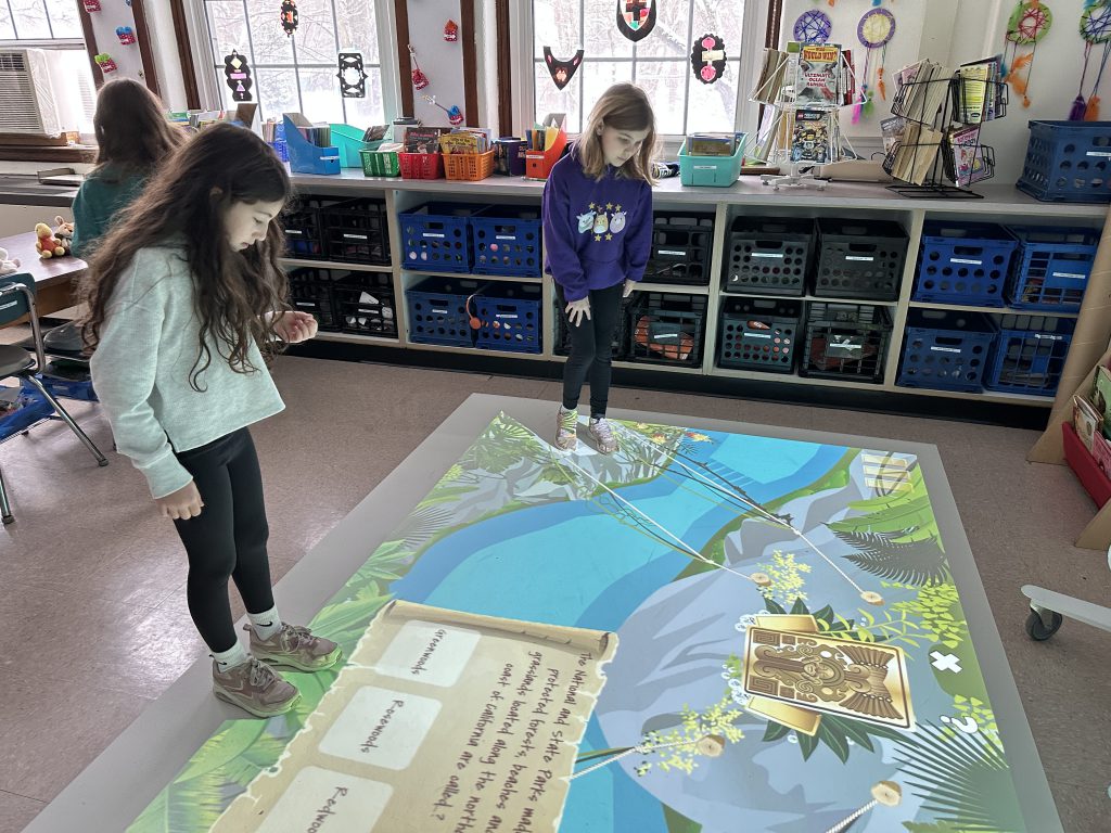 An image of two students standing and looking at a floor mat.