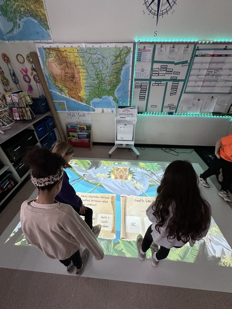 An image of students standing at the base of a floor mat where they are playing an educational game.