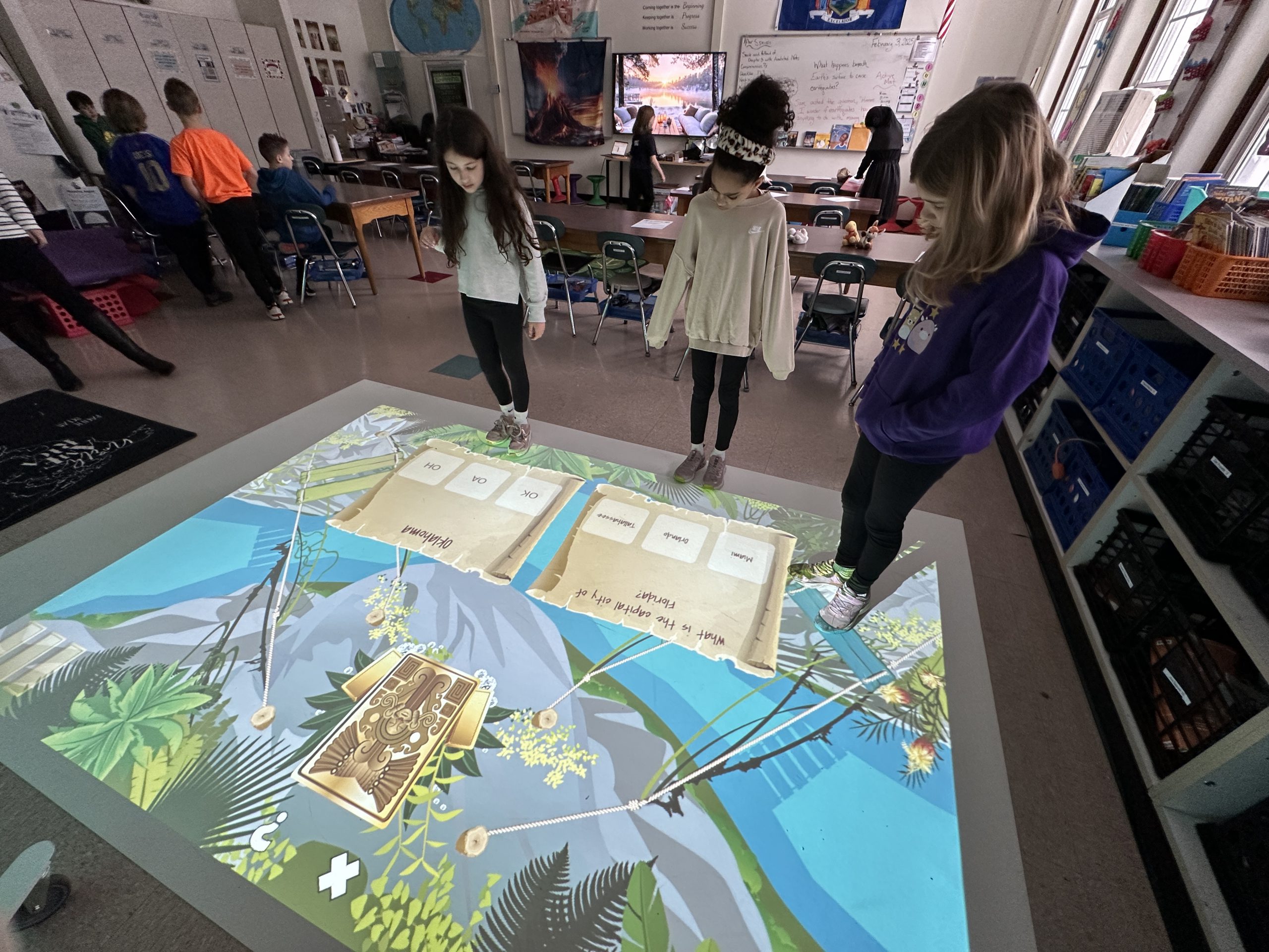 An image of three students standing and looking at a mat on the floor.