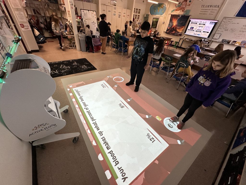 Two students standing at the base of a floor mat looking at a question.