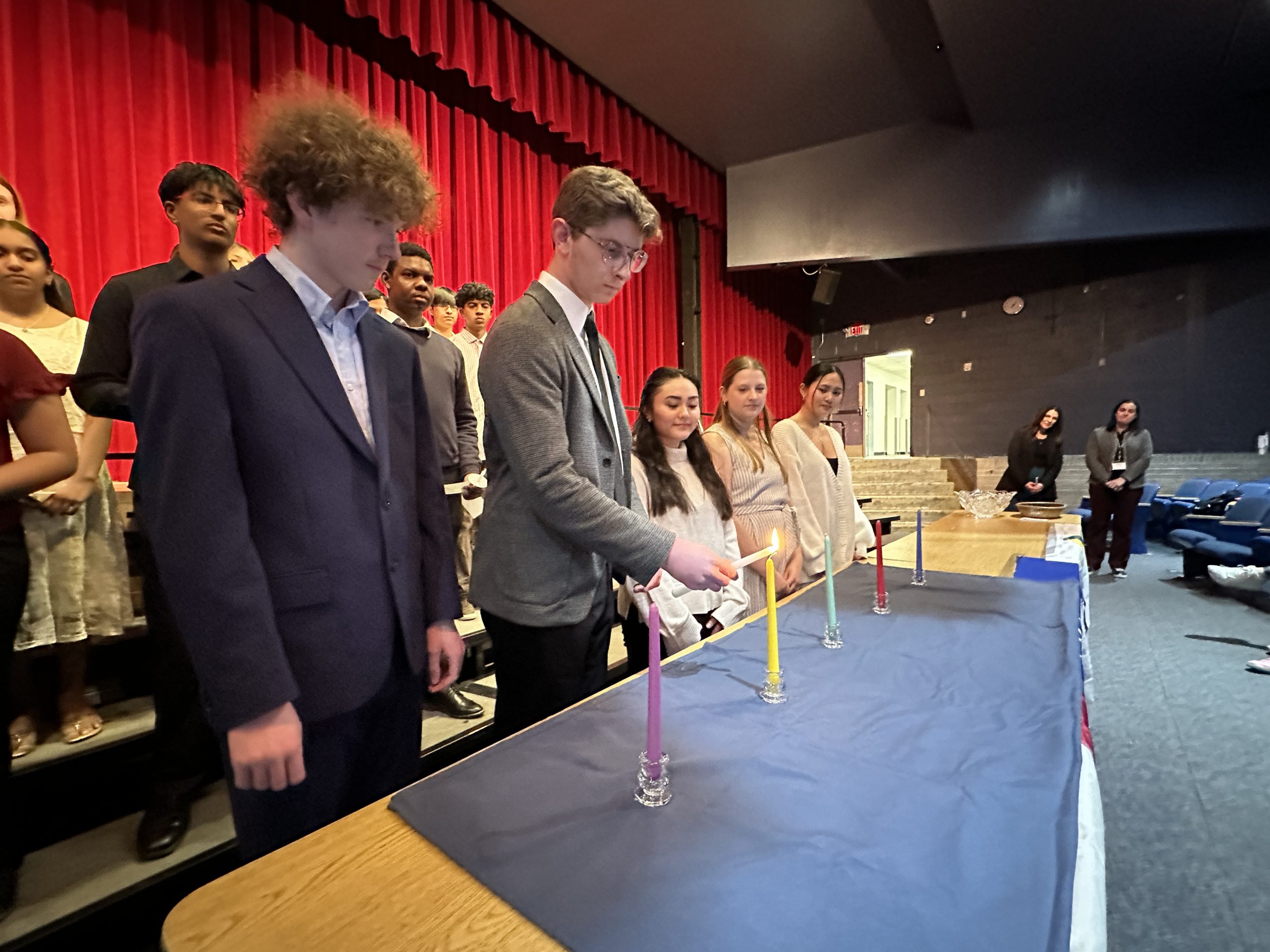 An image of students standing behind a table as one lights a candle.