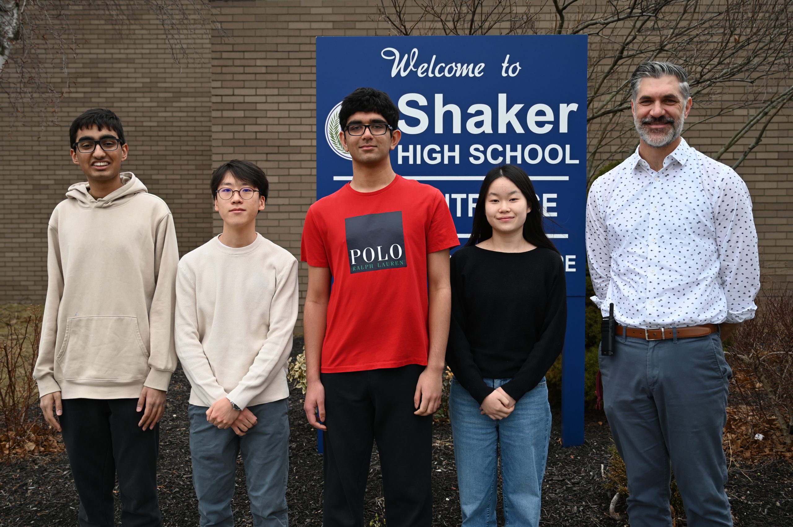 An image of four students standing with their Principal front of a Shaker High School entrance sign.