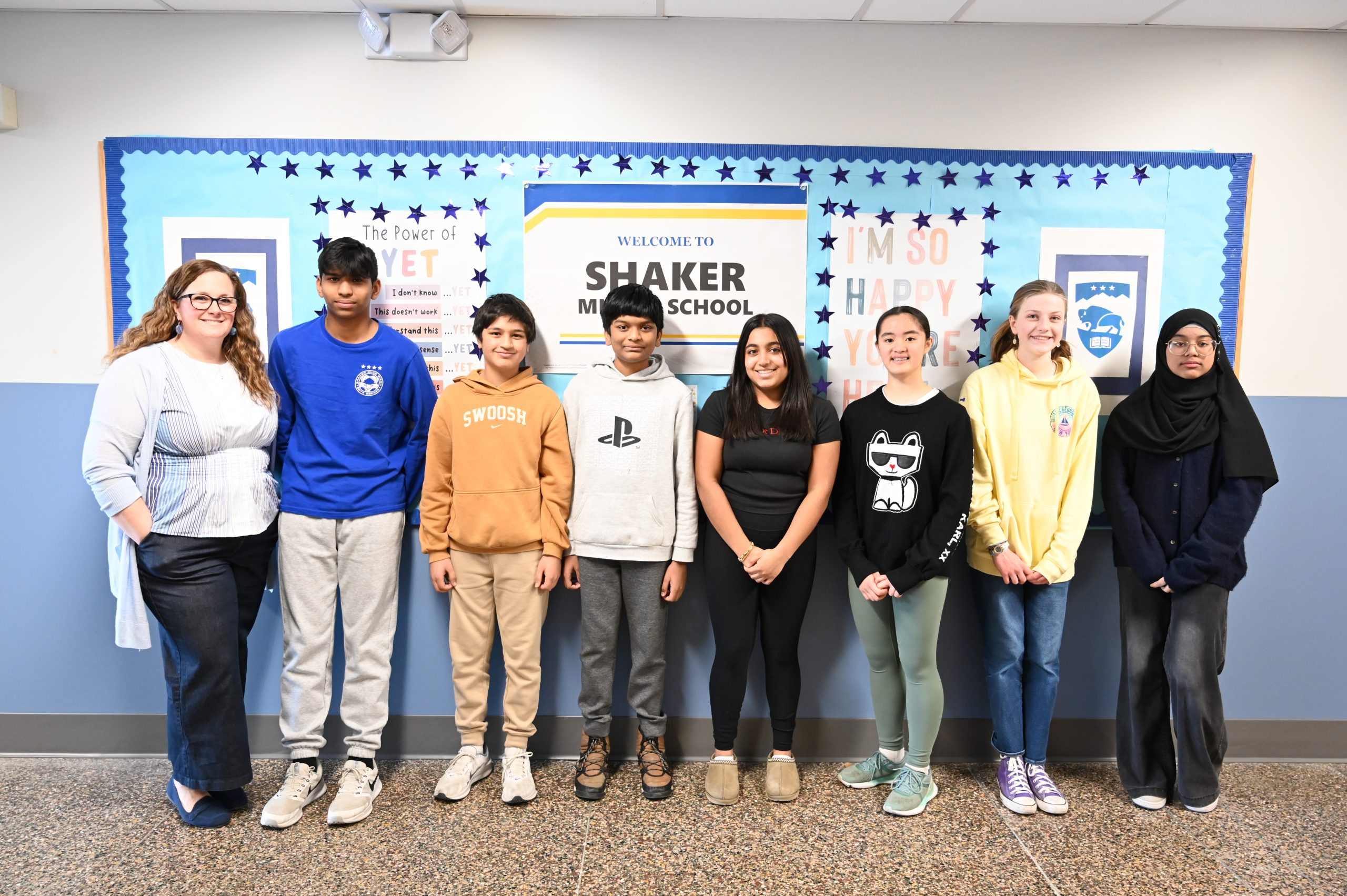 An image of a teacher and seven of her students posing in front of a bulletin board.