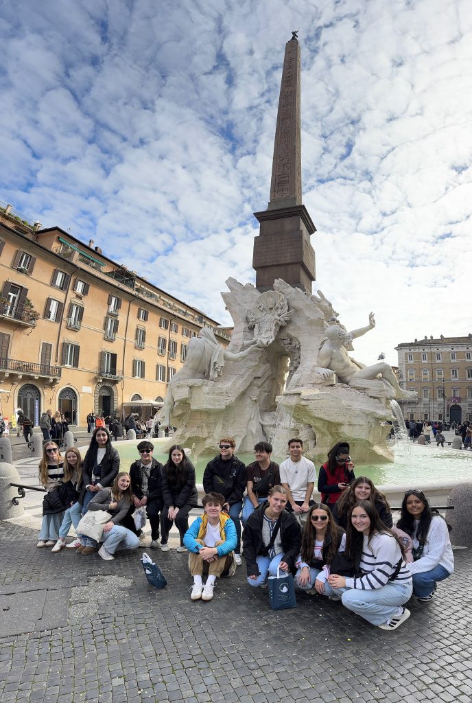 An image of students sitting in front of a large fountain with a sculpture in the middle of it.