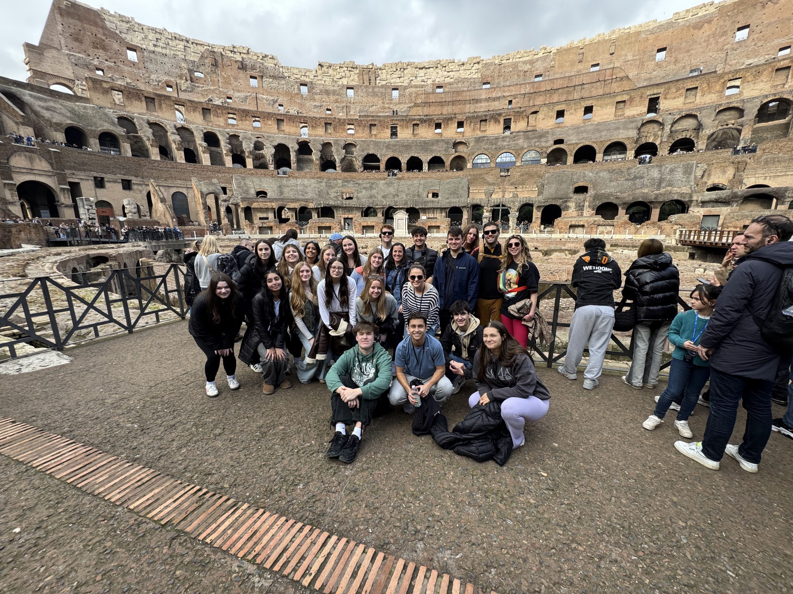 An image of a large group of students and several teachers posing in front of the Colosseum in Rome.