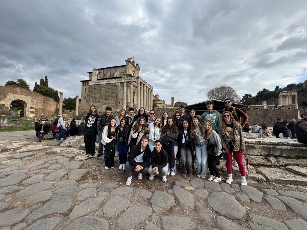 An image of a group of students posing in front of ancient ruins as others around them tour the grounds.