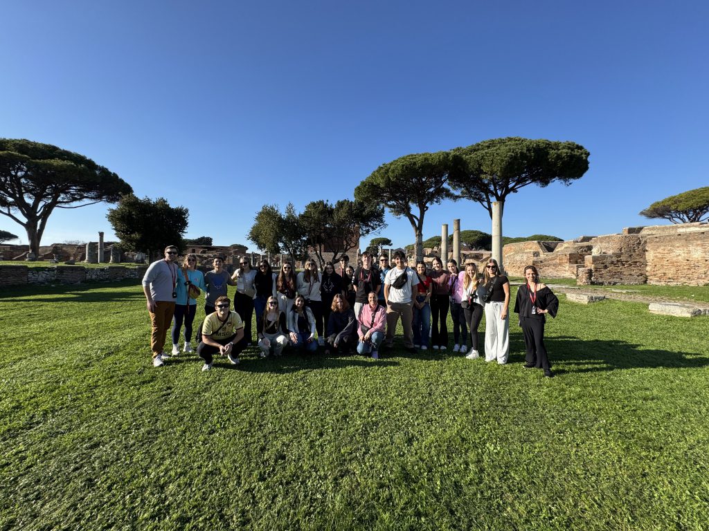 An image of a group of students standing in front of trees and ruins in Italy.